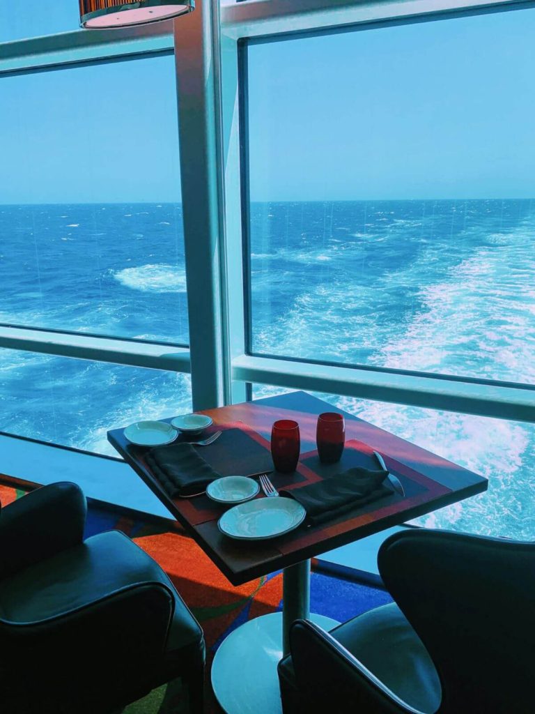 a dining table set for two overlooking the wake of a cruise ship