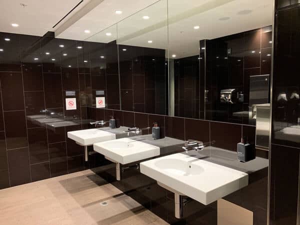 bathroom with 3 white sinks and a large mirror with brown wall tiles