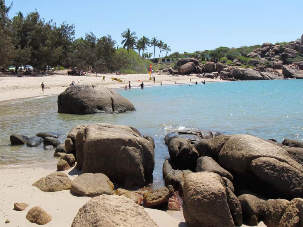 a sandy bay with surf lifesavers and people swimming in the ocean and relaxing on the beach