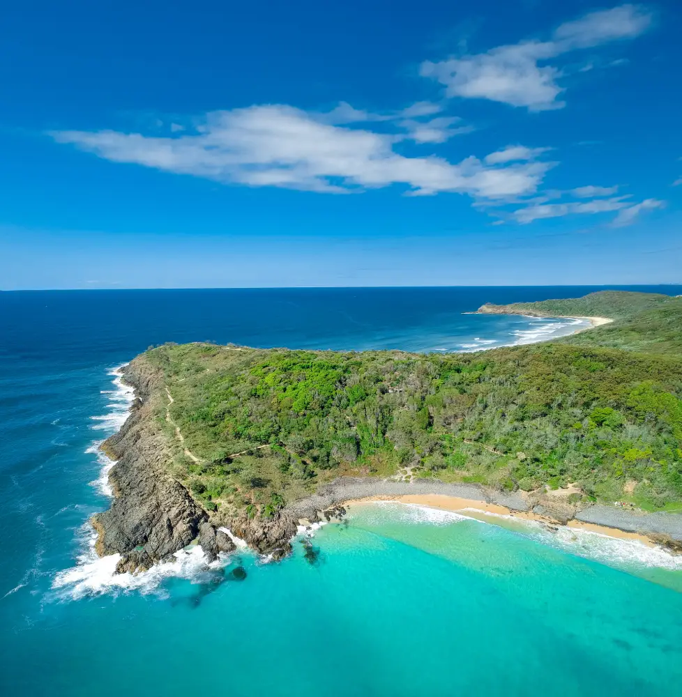 aerial view of a green headland and a sandy bay with turquoise water