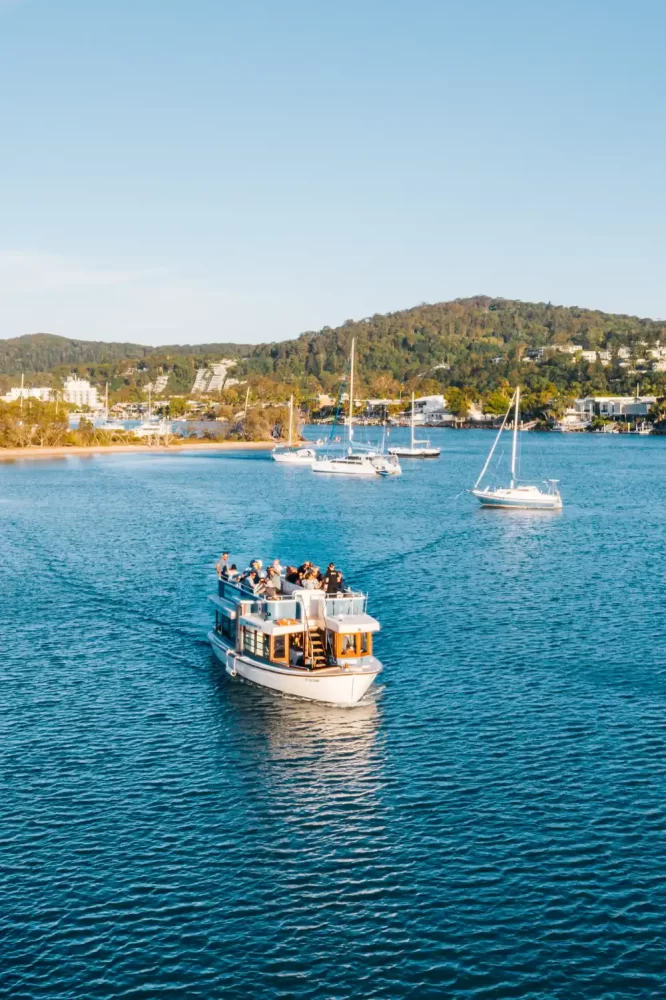 ferry with people on the top deck with views of the river and other boats at sunset