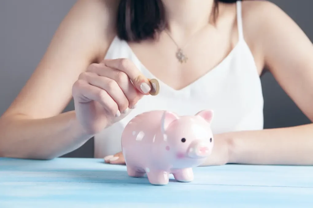 woman in white putting coins into pink piggy bank