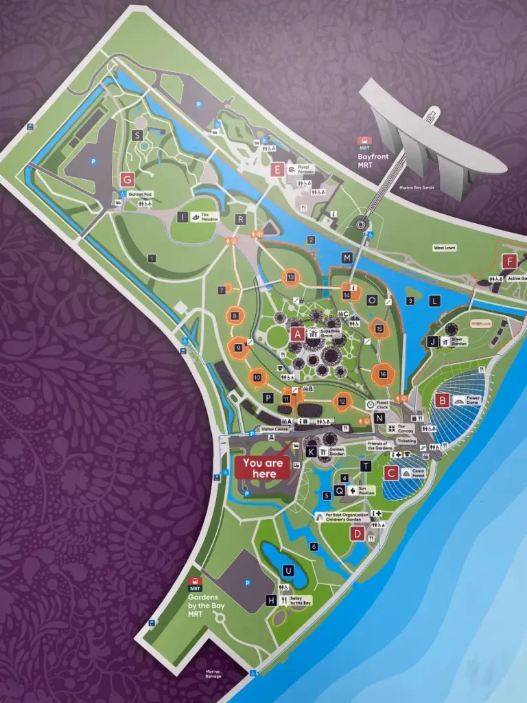 A detailed map of Gardens by the Bay in Singapore, displaying key attractions, walking paths, and facilities. The map highlights major landmarks such as the Flower Dome, Cloud Forest, Supertree Grove, and Bayfront MRT station, with a "You Are Here" marker indicating the current location. The layout includes water features, green spaces, and various activity zones for visitors.