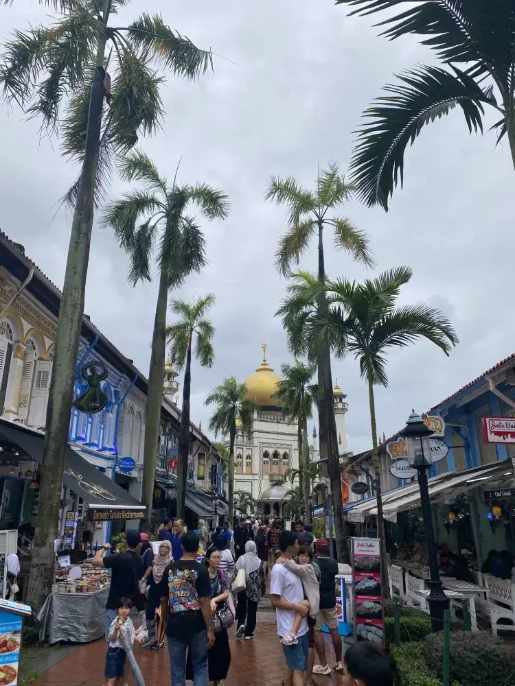 people wandering along the street in kampong gblam singapore. Shops and stalls line the street with the mosque in the background