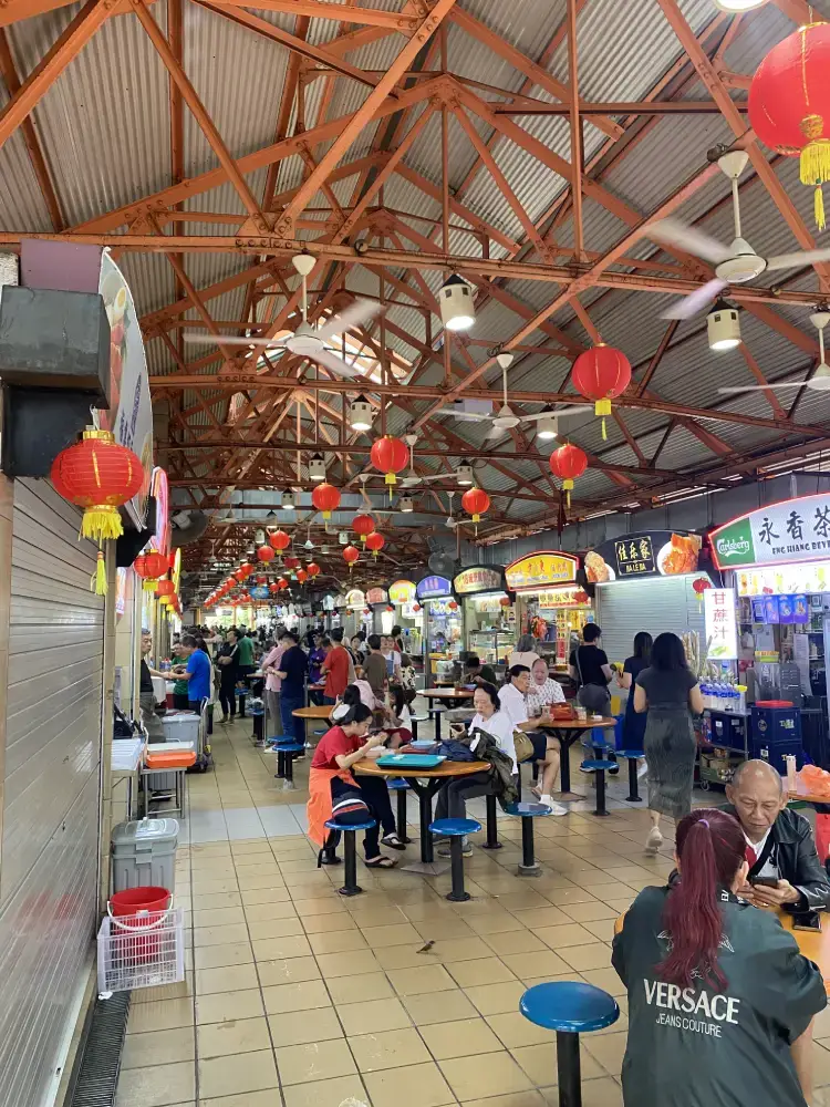 lots of people eating food at tables inside the maxwell centre hawker centre in singapofre chinatown. people queuing at tghe food stalls for their food